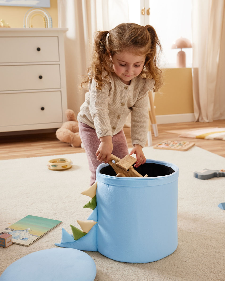 Laps paneb puidust mänguasju sinisesse dinosauruse-teemalisse hoiukasti.
