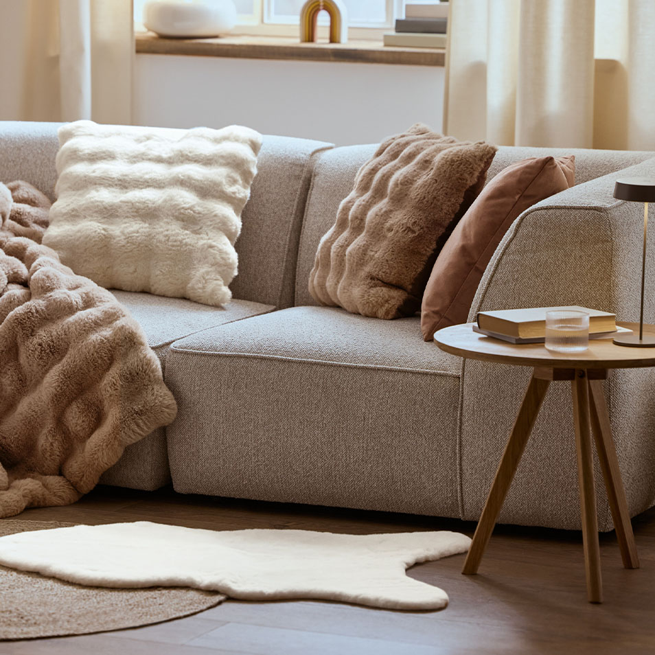 Hall mooduldiivan kohevate patjade ja tekiga, puidust külglaua kõrval.