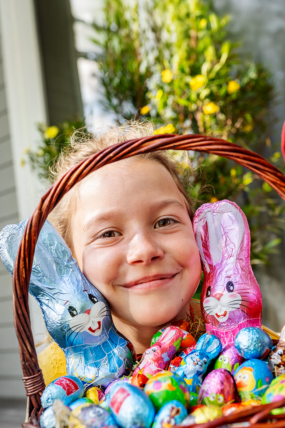 Naeratav tüdruk korviga, mis on täis šokolaadist lihavõttejäneseid ja mune.