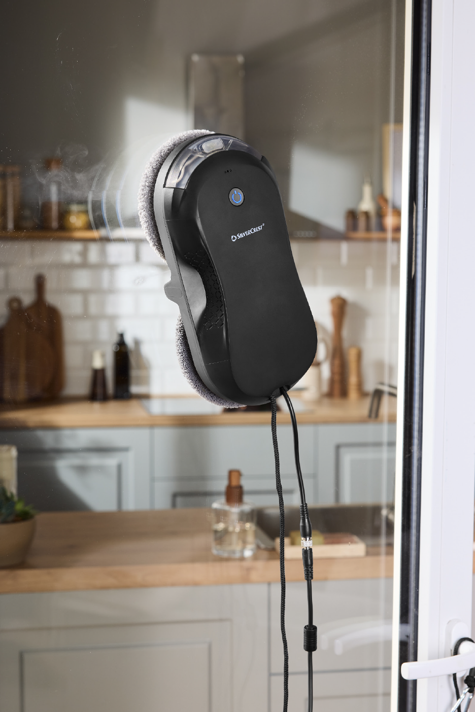 Aknapesurobot puhastab köögiakent, taustal näha puidust tööpind ja kapid.