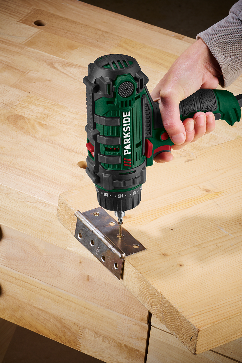 Inimene kasutab akutrelli puidust lauale hinge kinnitamiseks.