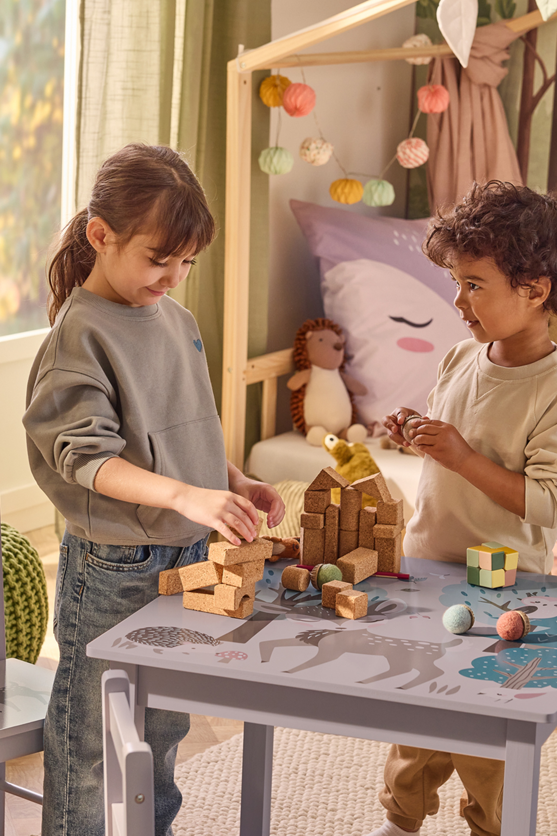 Kaks last mängivad puidust klotside ja mänguasjadega laste laua taga.