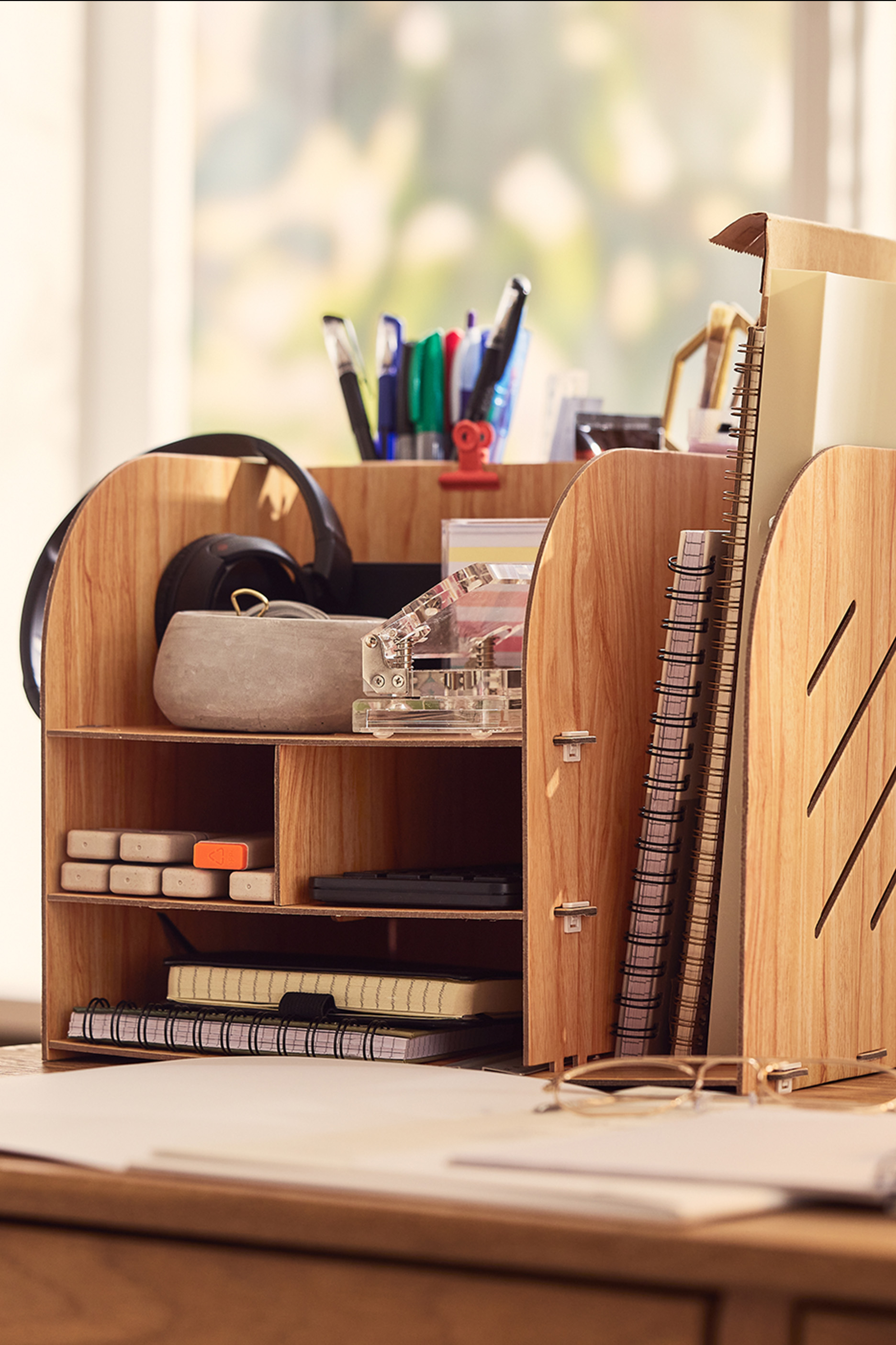 Puidust lauakorraldaja kirjatarvete, märkmike ja kõrvaklappidega laual.