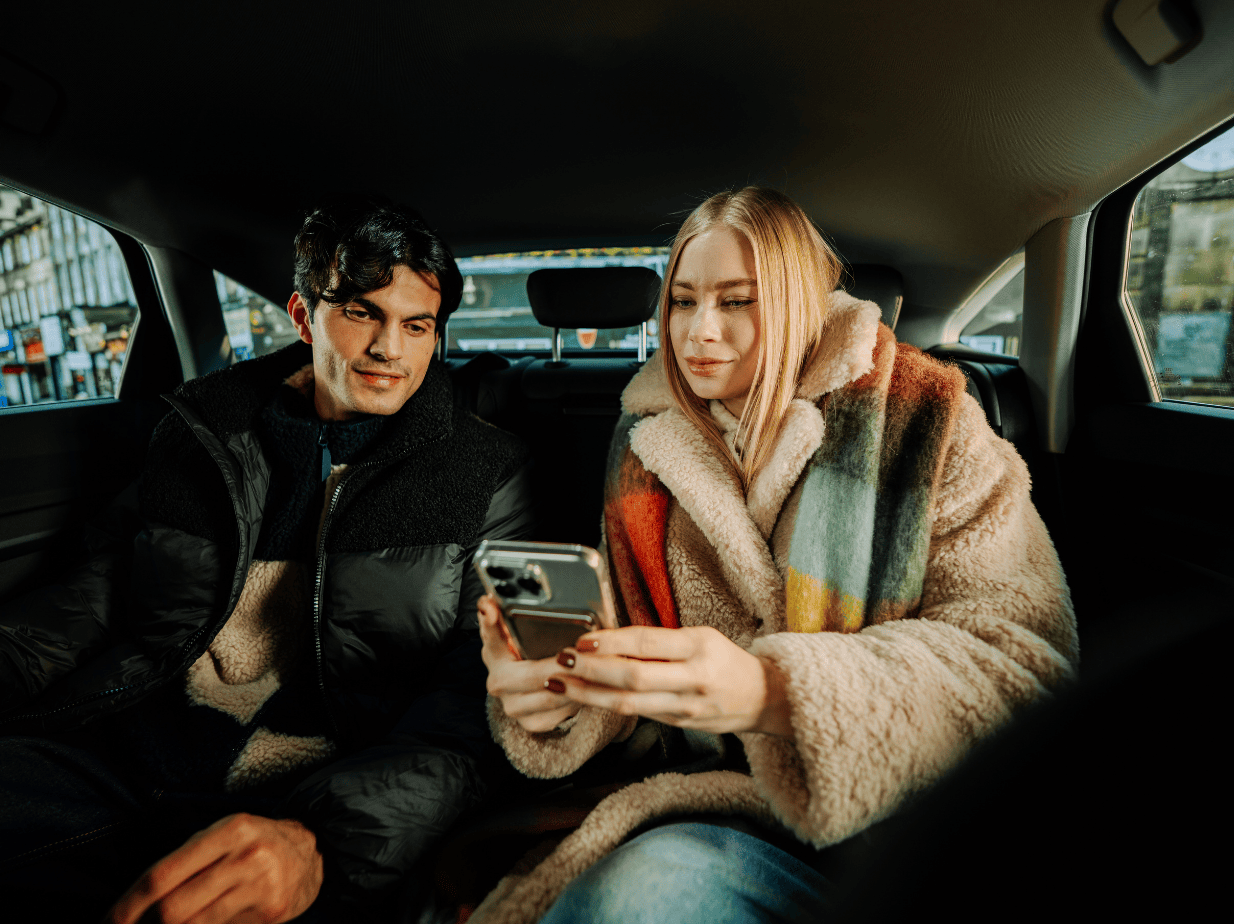 Paar kasutab taksos nutitelefoni; naisel on karvmantel.